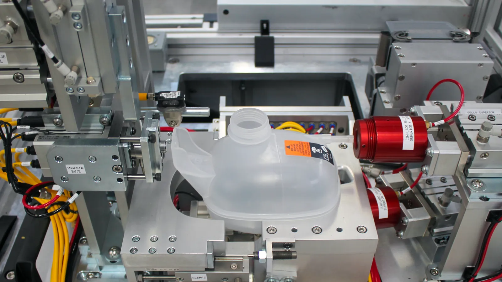 Machined aluminum nest holding a plastic reservoir, with red inflatable seal heads at its ports, built by AMD Machines