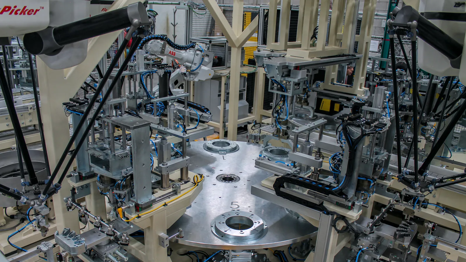 Two delta robots, one an ABB FlexPicker, around a rotary dial machine with part nests, built by AMD Machines