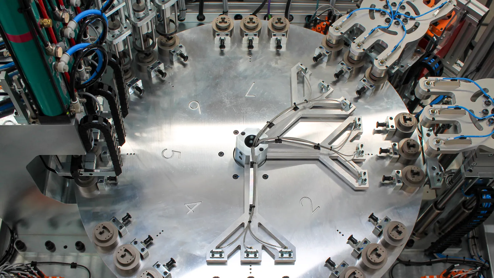 Overhead view of a custom rotary-dial assembly machine with three-up nests and pneumatic stations, built by AMD Machines
