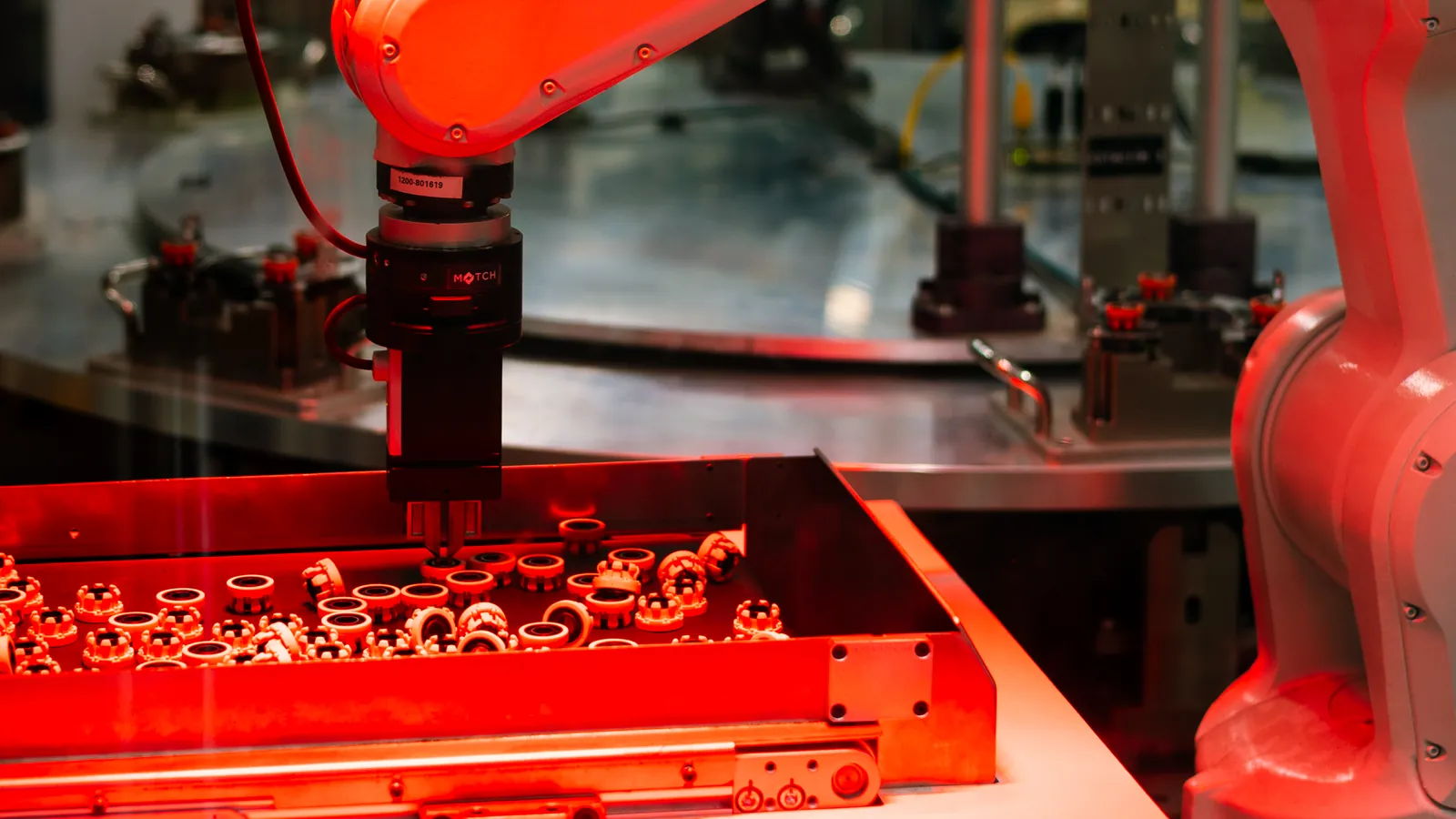 Robot gripper picking randomly oriented loose parts from a red-lit tray beside a dial table, built by AMD Machines