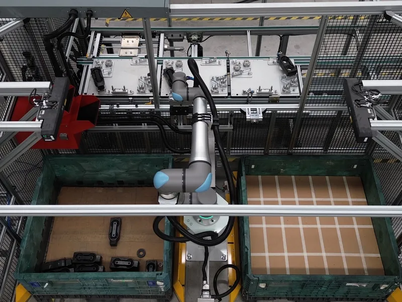 Cobot bin picking cell with vision sensors over two bulk part bins and a fixture pallet conveyor, built by AMD Machines