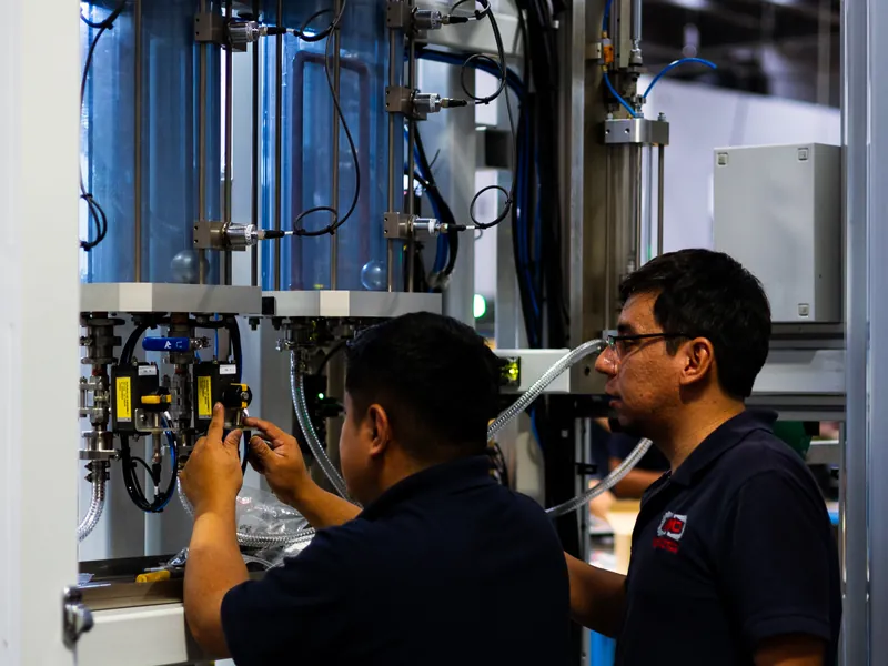AMD Machines engineers adjusting actuated valves below clear fluid columns fitted with level sensors