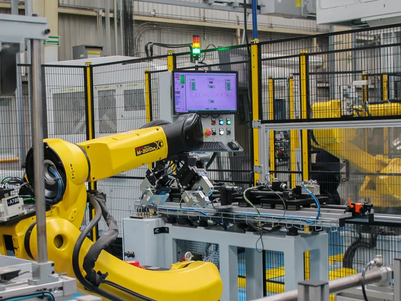 FANUC robot with a dual gripper at a pneumatic fixture rail, with HMI and stack light, in a cell built by AMD Machines
