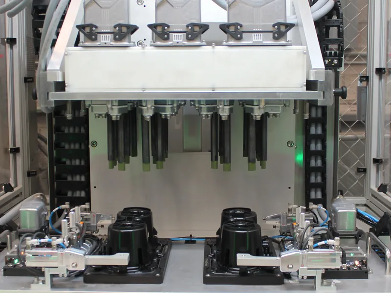 Multi-probe heat staking head above four black plastic housings held in clamped fixture nests, built by AMD Machines