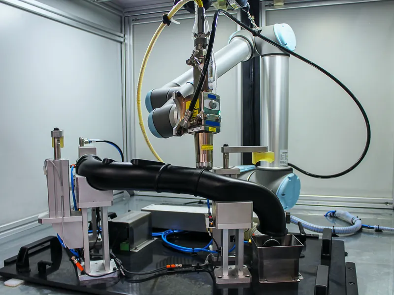 Universal Robots cobot holding a laser processing head over a fixtured part in an enclosed laser cell, built by AMD Machines