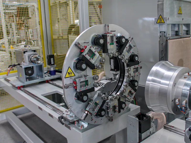 Ring fixture with radial rack-and-pinion slides and guide rollers beside machined round tooling, built by AMD Machines