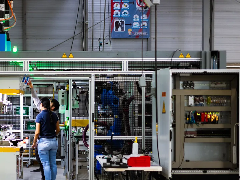 AMD Machines team members at a guarded robotic cell with its control cabinet open, on the Querétaro shop floor