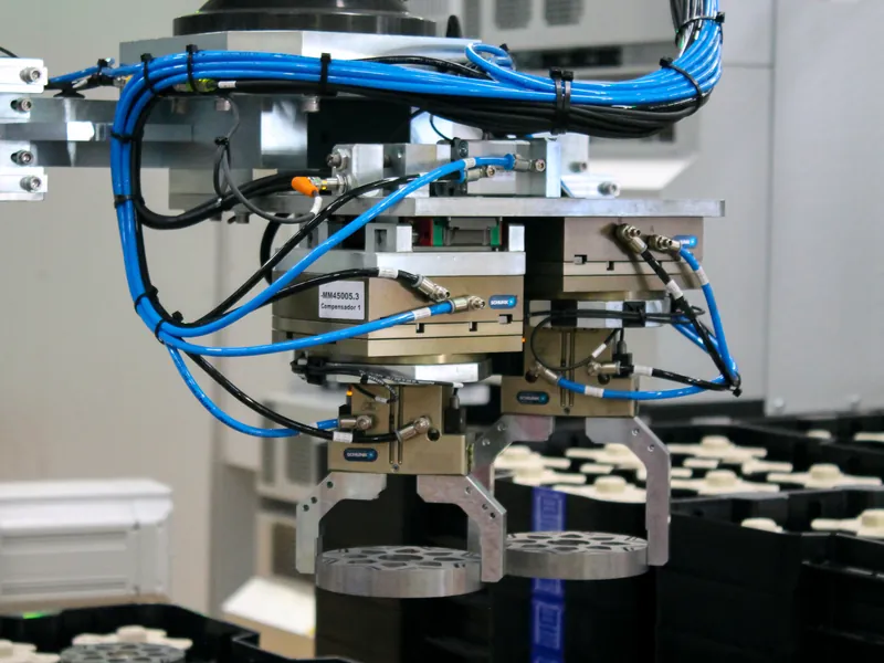 Pick-and-place tool with two SCHUNK grippers holding perforated metal discs above parts trays, built by AMD Machines