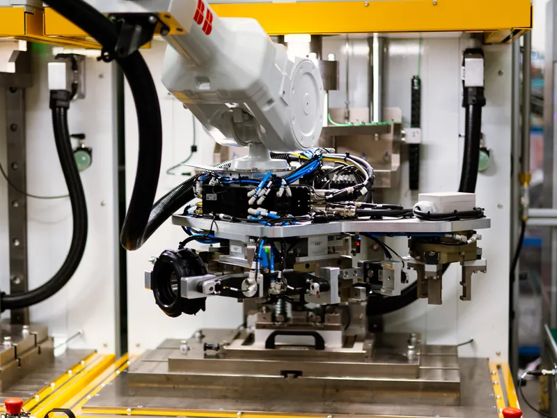 ABB robot with a multi-gripper end-of-arm tool holding a rubber-metal part above a station fixture, built by AMD Machines