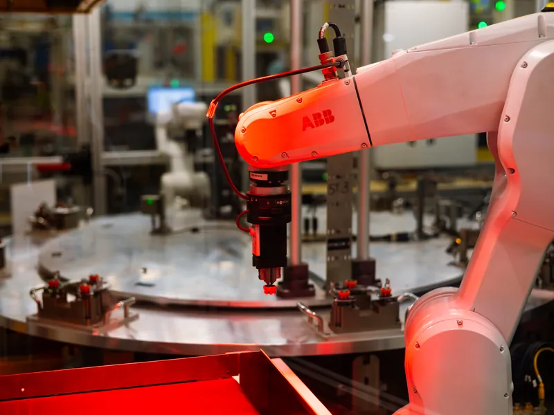 ABB robot with a gripper holding a part above the nests of a rotary dial assembly machine, built by AMD Machines