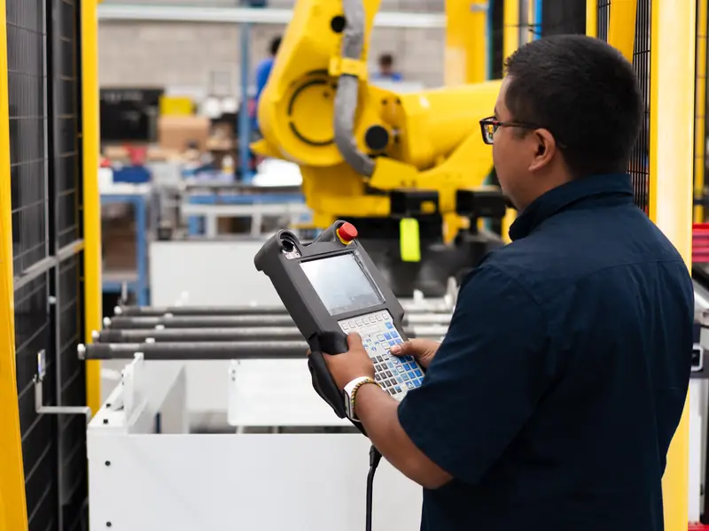 AMD Machines technician working on a FANUC robot with a teach pendant